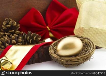 Gold egg in twig nest with holiday red bow and pine cones in wood box offers a rustic view of financial savings and investment. Gift of start or addition to portfolio is concept.