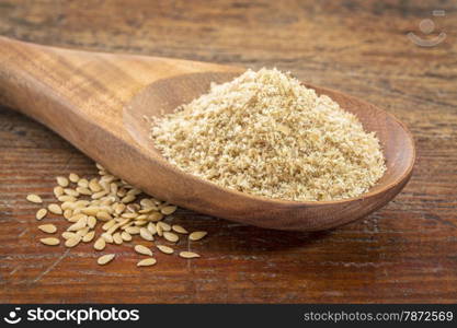 gold flax meal on a wooden spoon with seeds against a grunge wood