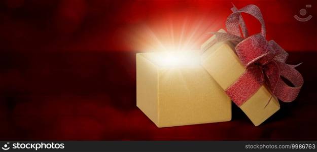 Gold gift box with ribbon open and light blurred bokeh background, present with luxury for love and anniversary with glowing and sparkle in festive, copy space, Valentine day or Christmas concept.