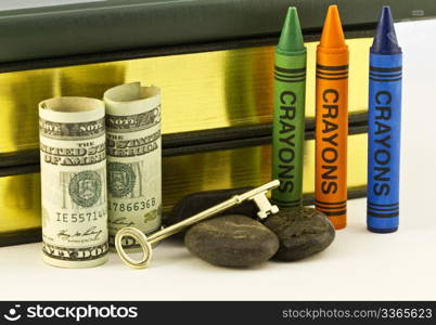 Gold key is placed on rocks that are next to money and crayons with books behind. Although education is the key to the future, many schools are having rocky financial times.