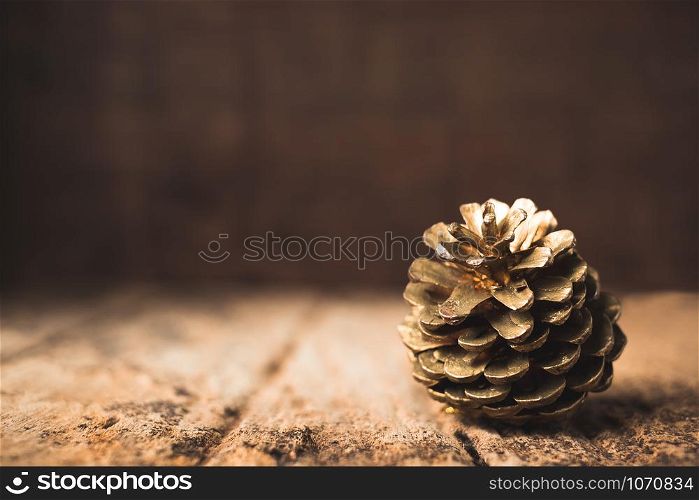 gold pine cone on grunge wood table and dark brown wooden wall.Winter Merry Christmas holiday greeting card.