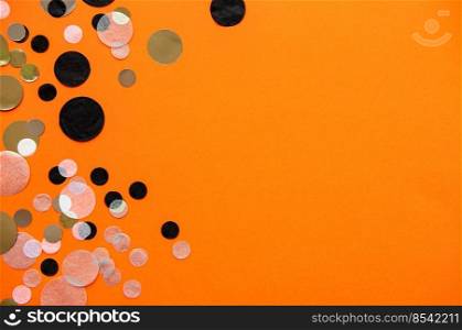 Gold, silver, black and white foil confetti sparse on orange background. Simple halloween holiday concept. Copy space for text. Top view, flat lay