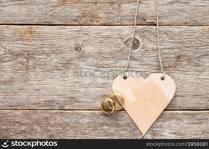 Gold wedding rings and paper heart nanging on wooden background