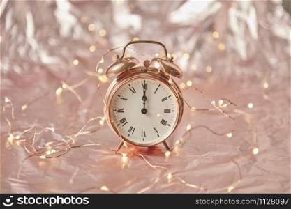 Golden alarm clock with time is midnight on a shiny cooper abstract background with string of lights, copy space. Greeting card.. Christmas exact time on an old-fashioned cooper alarmclock.