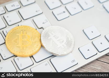 Golden and silver bitcoins lying on a white keyboard . Golden and silver bitcoins on a keyboard