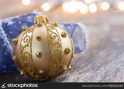 golden ball with blue ribbon on wooden table, christmas defocused lights in background