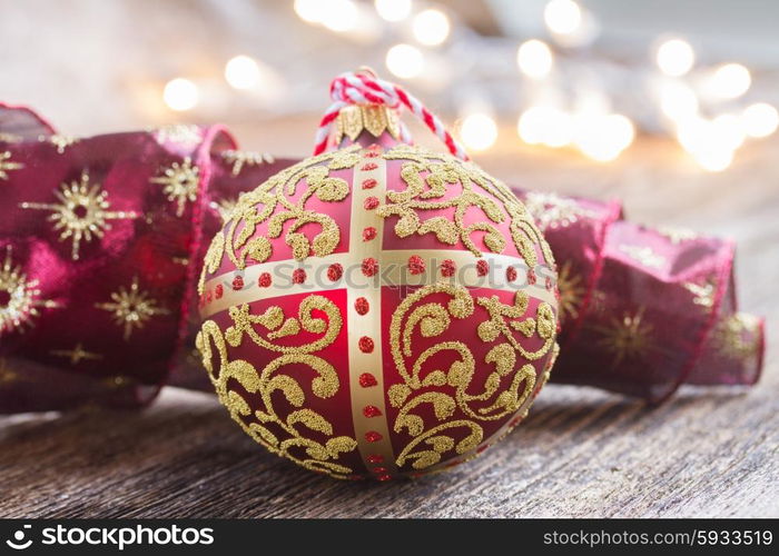 golden ball with red ribbon on wooden table, christmas defocused lights in background