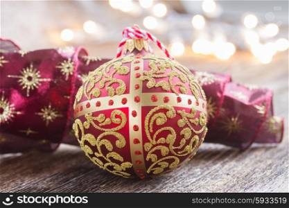 golden ball with red ribbon on wooden table, christmas defocused lights in background