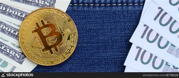Golden Bitcoin, dollar and euro bills lies on a blue jeans fabric. New virtual money. New crypto currency in the form of the coins