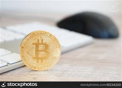Golden bitcoin on a wooden desk near white keyboard and computer mouse. Electronic money mining concept. Golden bitcoin on a wooden desk