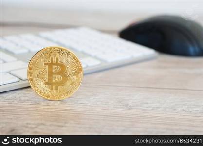 Golden bitcoin on a wooden desk near white keyboard and computer mouse. Electronic money mining concept. Golden bitcoin on a wooden desk