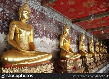 Golden Buddhas near the wall in corridor, wat Suthat, Bangkok, Thailand