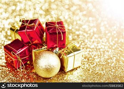 Golden Christmas ball and red gifts on abstract glitter background