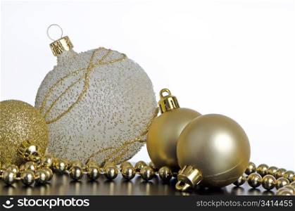 Golden christmas balls with decorations on black surface and white backdrop.
