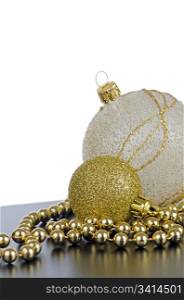 Golden christmas balls with decorations on black surface and white backdrop.