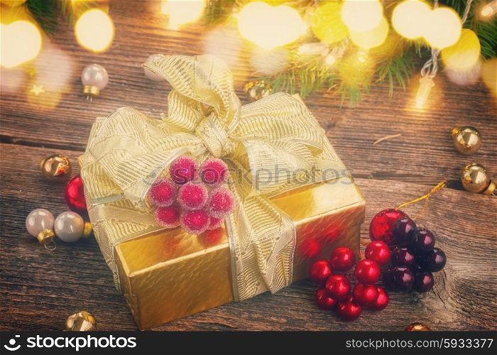 golden christmas gift box with lights on evergreen tree in background on wooden table, retro toned