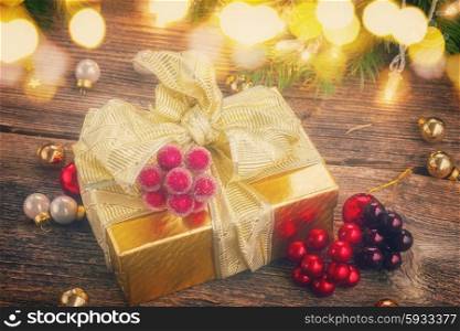 golden christmas gift box with lights on evergreen tree in background on wooden table, retro toned