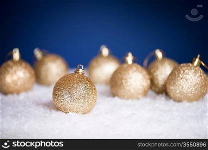 Golden Christmas tree decorations on snow against dark blue background