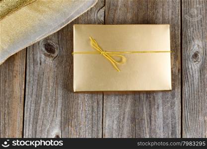 Golden color wrapped gift box and ribbon on rustic wood. Holiday concept of giving.
