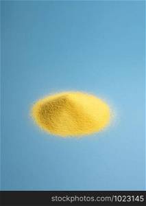 Golden corn flour pile on a blue paper background. Freshly grounded maize. Cooking ingredient for polenta and cornbread. Raw corn products.