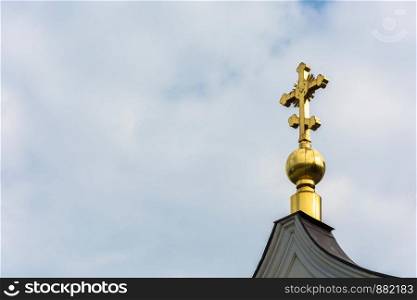 Golden cross on a small Golden dome on the background of cloudy sky.