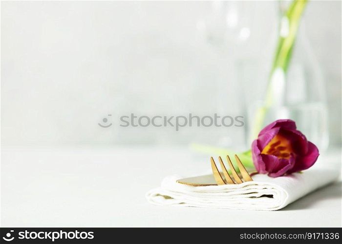 Golden Cutlery set and beautiful flower on light grey table with space for text. Festive table setting