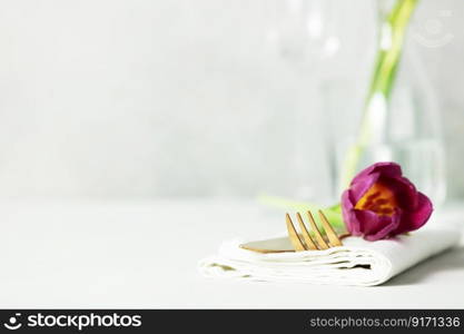 Golden Cutlery set and beautiful flower on light grey table with space for text. Festive table setting