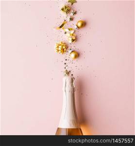 Golden decoration of ribbon, stars, Christmas balls and confetti flying from bottle of champagne. Flat lay. Festive concept.. Flat lay of Celebration. Champagne bottle and golden decoration on pink background
