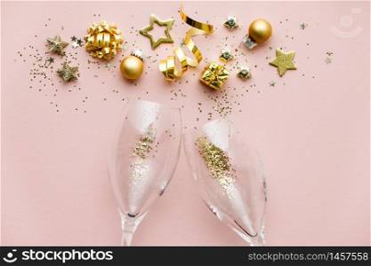 Golden decoration of ribbon, stars, Christmas balls, confetti and champagne glasses on pink background. Flat lay. Festive concept.