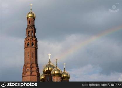 Golden domes of the Resurrection Cathedral against a cloudy sky and rainbow in the city of Vichuga, Ivanovo region, Russia.