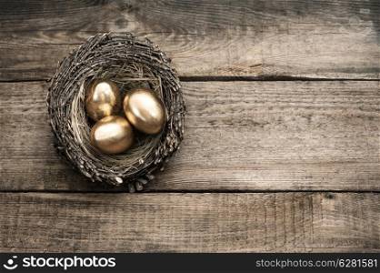 golden easter eggs in birds nest on vintage wooden background
