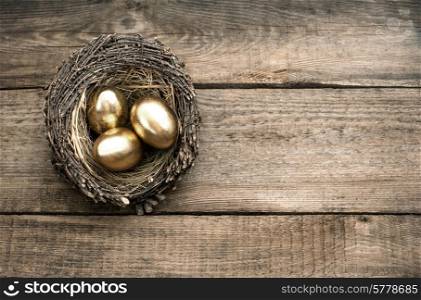 golden easter eggs in birds nest over rustic wooden background