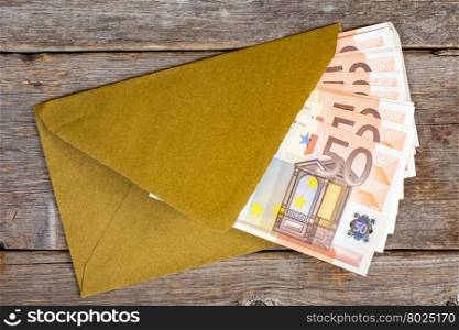 Golden envelope with Euro bills over wooden background