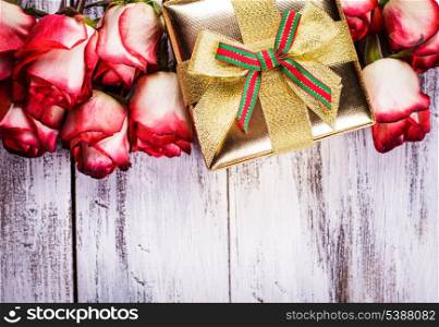 Golden gift box and bouquet of roses on white shappy painted wooden background