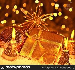 Golden gift box with baubles decorations and candles, Christmas tree ornament for winter holidays, present with abstract bokeh shiny glowing blur lights background