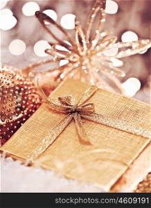 Golden gift box with baubles decorations, Christmas tree ornament for winter holidays, present with abstract bokeh shiny glowing blur lights background