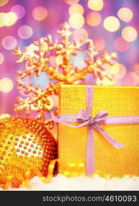 Golden gift box with baubles decorations, Christmas tree ornament for winter holidays, present with purple abstract bokeh shiny glowing blur lights background