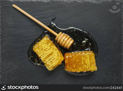 Golden honeycomb and honey stick on a black stone slate plate. Top view