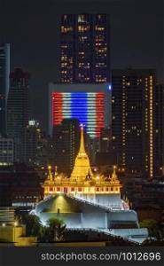 Golden Mount or Wat Saket, Phukhao Thong, and skyscraper buildings with Thailand flag at night in Bangkok City, Thailand. Buddhist temples.