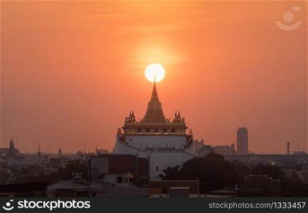Golden Mountain pagoda, a buddhist temple or Wat Saket with the sun in Bangkok Downtown, urban city with sunset sky, Thailand. Thai architecture landscape background.