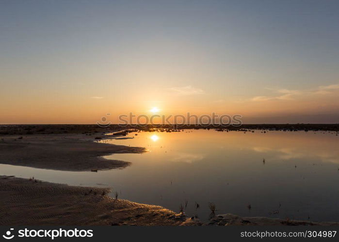 Golden natural small lake or pond sunset view of blue and orange sky landscape. Sunset or sunrise reflection in nature with sun in clouds above small water lake or pond. Golden natural small lake or pond sunset view