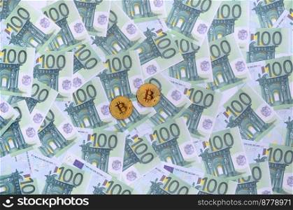 Golden physical bitcoins is lies on a set of green monetary denominations of 100 euros. A lot of money forms an infinite heap