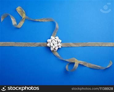 golden ribbon crossed on a dark blue background in the middle of a gray bow, imitation of tying a gift, top view