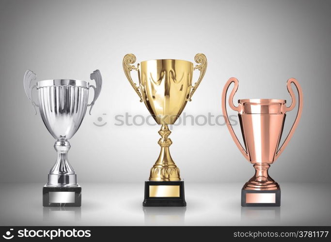 golden, silver and bronze trophies on gray background