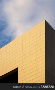 Golden sunlight on surface of modern office building wall against white clouds with blue sky at morning time in perspective view and vertical frame