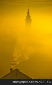 Golden sunrise church tower in fog and chimney smoke in town of Krizevci, Prigorje region, Croatia