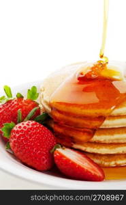 Golden syrup drizzling down over hot buttered pancakes with a strawberry garnish.