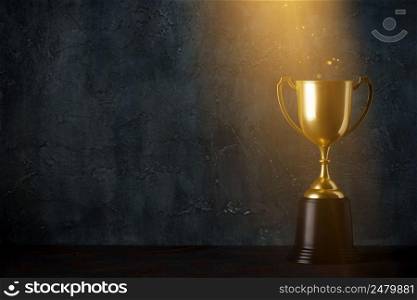 Golden trophy cup on dark table with rays of light and glitter dust dark background with copy space