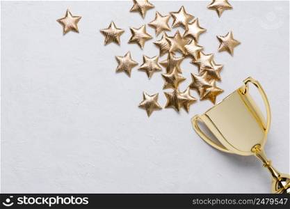 Golden winner trophy cup with golden stars on white textured background with copy-space