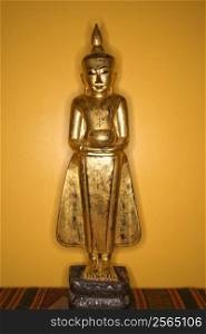 Golden wooden Buddha statue from Myanmar against yellow wall.